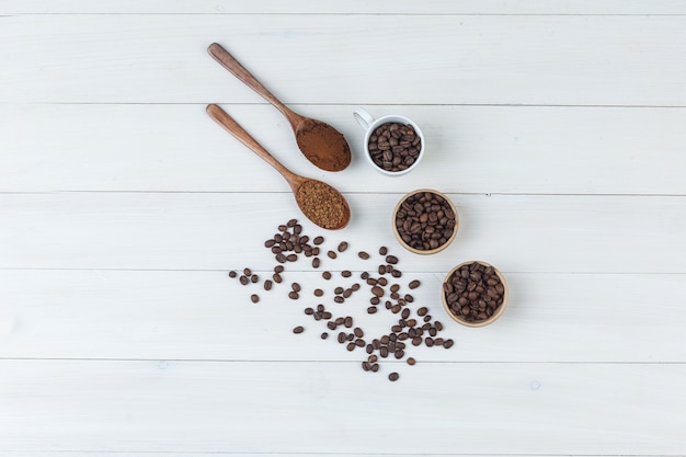 Algunos granos de café con café molido en taza y tazones sobre fondo de madera, vista superior.