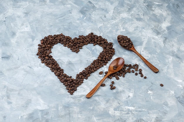 Algunos granos de café en cucharas de madera sobre fondo de yeso gris, plano laical.