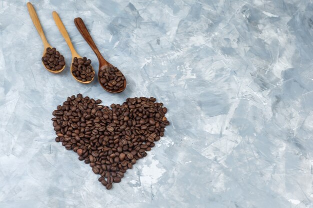 Algunos granos de café en cucharas de madera sobre fondo de yeso gris, plano laical.