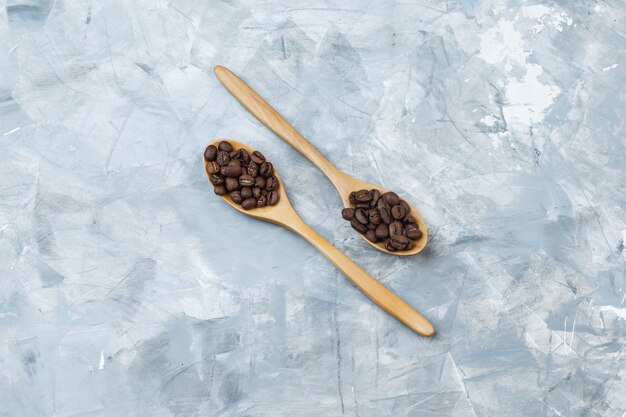 Algunos granos de café en cucharas de madera sobre fondo de yeso gris, plano laical.