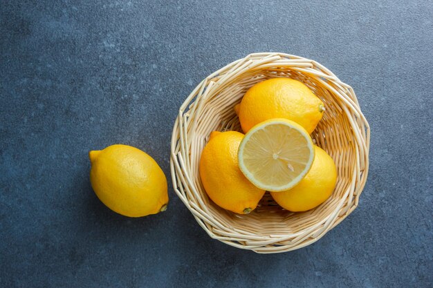 Algunos limones amarillos en una canasta sobre una superficie oscura, vista superior.