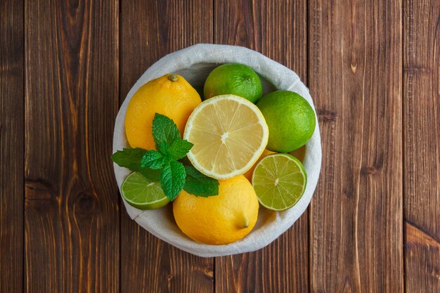 Algunos limones en una canasta sobre la superficie de madera, vista superior.