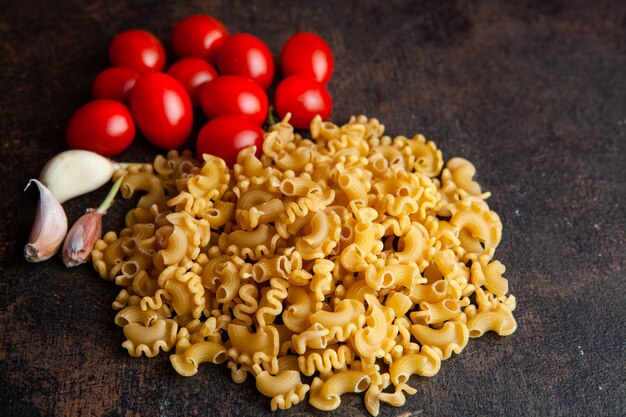 Algunos macarrones con tomates y ajo sobre fondo oscuro con textura, vista de ángulo alto.