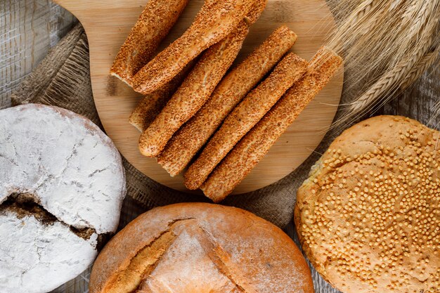 Algunos productos de panadería con cebada en la tabla de cortar y superficie de madera, vista desde arriba.