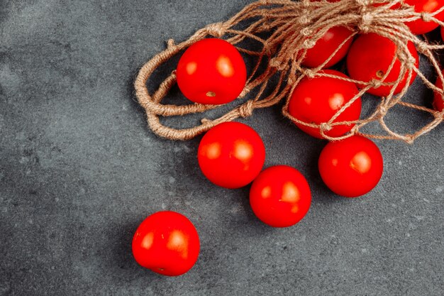 Algunos tomates en una bolsa neta sobre fondo oscuro con textura, vista de ángulo alto.