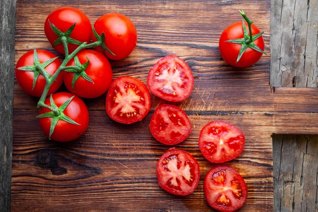 Algunos tomates y rodajas con cuchillo en una tabla de cortar de madera vista desde arriba.