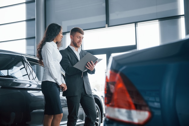 Algunos tratos serios. Clienta y empresario barbudo con estilo moderno en el salón del automóvil