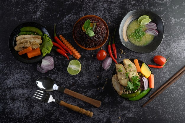 Alimentos variados y platos de verduras, carne y pescado en una mesa de piedra negra. Vista superior.