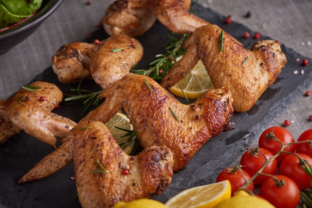 Alitas de pollo asadas en salsa barbacoa con semillas de pimiento Romero, sal en un plato de piedra negra sobre una mesa de piedra gris.