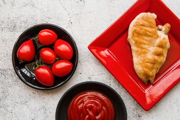 Alitas de pollo deliciosas en placa con el tomate y la salsa sobre fondo concreto