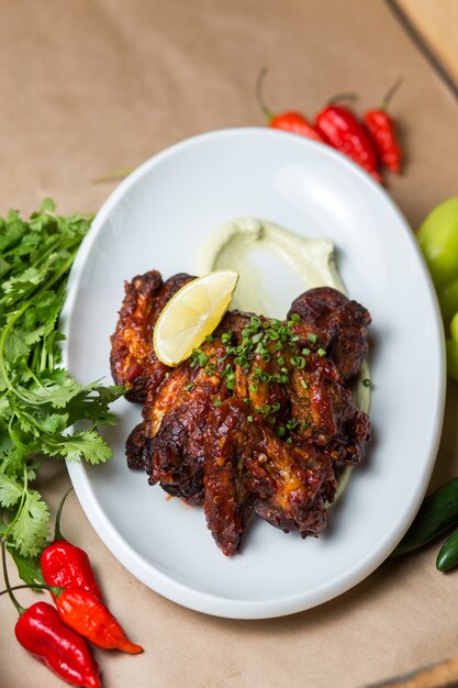 Alitas de pollo fritas adornadas con cebolla verde picada, salsa y rodaja de limón