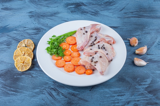 Alitas de pollo marinadas y diversas verduras en un plato sobre la superficie azul