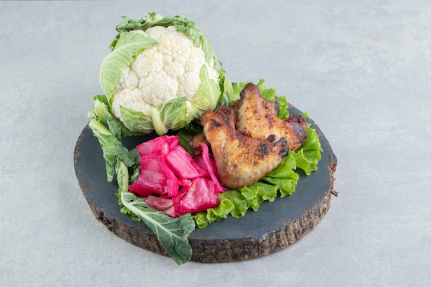 Alitas de pollo a la plancha y coliflor sobre pieza de madera.