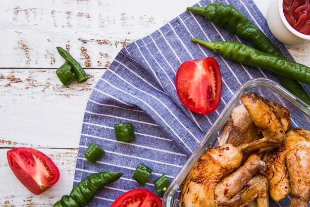 Alitas de pollo a la plancha y rodajas de tomate; chiles verdes en mesa de madera