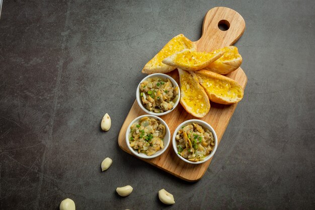 Almeja al horno con ajo y mantequilla servida con pan de ajo sobre fondo oscuro