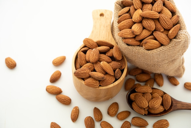 Almendra en cuchara de madera y cuenco. Saco con almendra sobre fondo blanco.