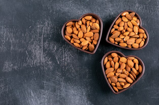 Almendra en cuencos en forma de corazón sobre una mesa de piedra negra. aplanada