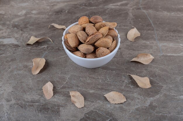 Almendras en un bol y hojas sobre la superficie de mármol.