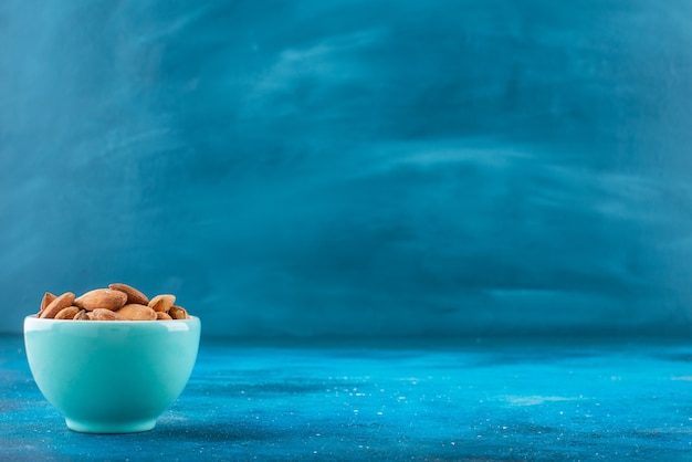 Almendras sin cáscara en un cuenco, sobre la mesa azul.