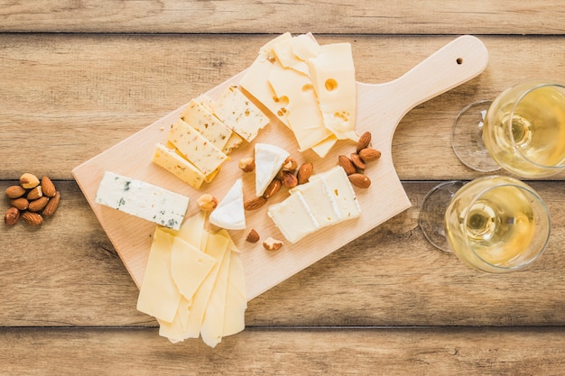 Almendras y diferentes tipos de queso con vino en mesa de madera.