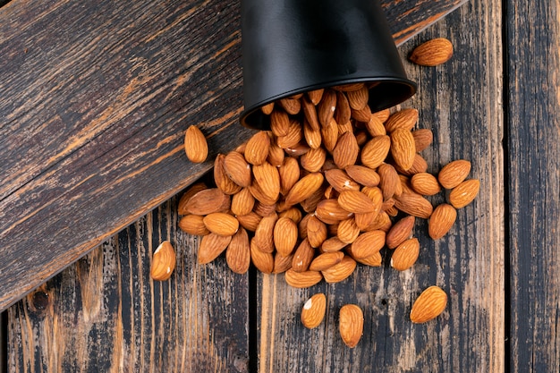 Almendras dispersas en un cubo negro sobre una mesa de madera oscura. vista superior.