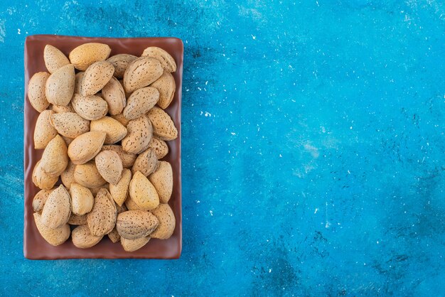 Almendras peladas en un plato, sobre la mesa azul.