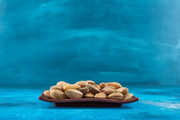 Almendras peladas en un plato, sobre la mesa azul.