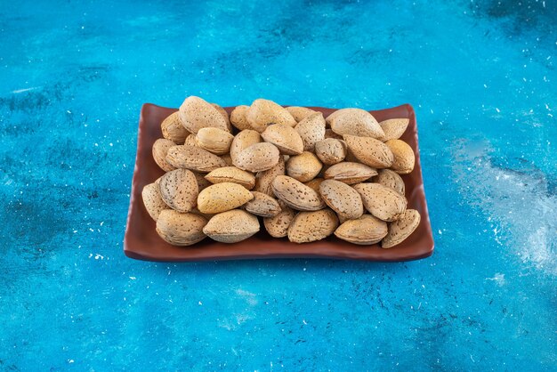 Almendras peladas en un plato, sobre la mesa azul.