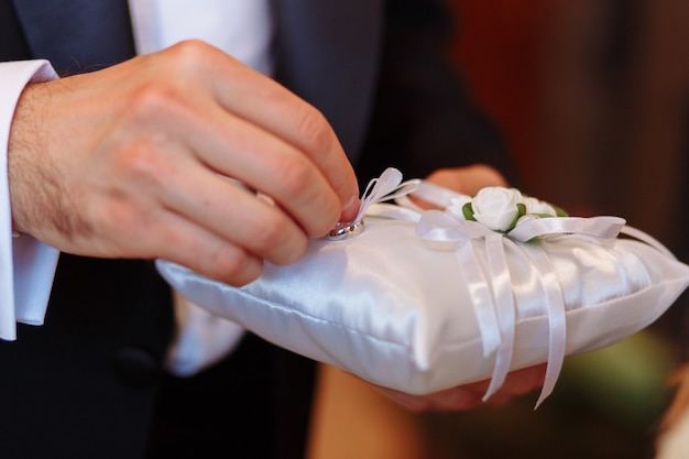 Almohada con anillos de boda. Novio tomando anillo durante la ceremonia