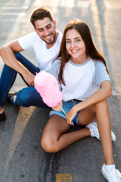 Alta vista pareja sentada en la carretera comiendo algodón de azúcar