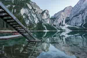 Foto gratuita altas montañas rocosas reflejadas en el lago braies con escaleras de madera cerca del muelle en italia