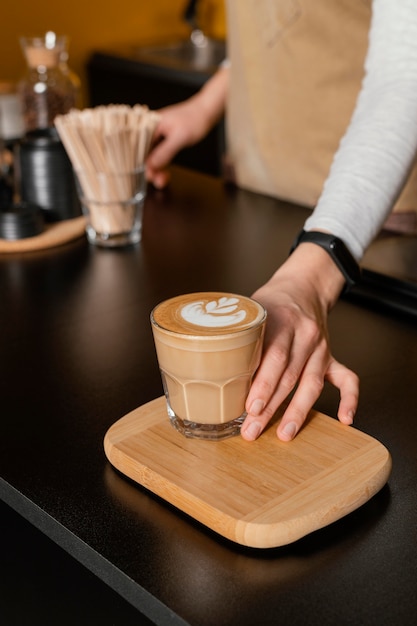 Alto ángulo de barista femenina sosteniendo un vaso de café decorado