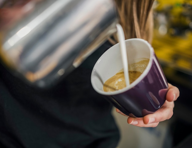 Alto ángulo de barista hembra vertiendo leche en café