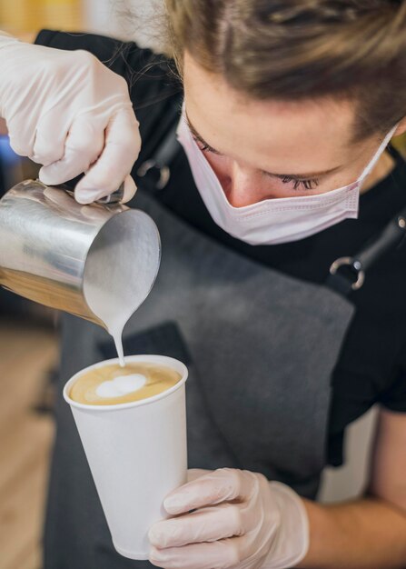 Alto ángulo de barista hembra vertiendo leche en la taza de café
