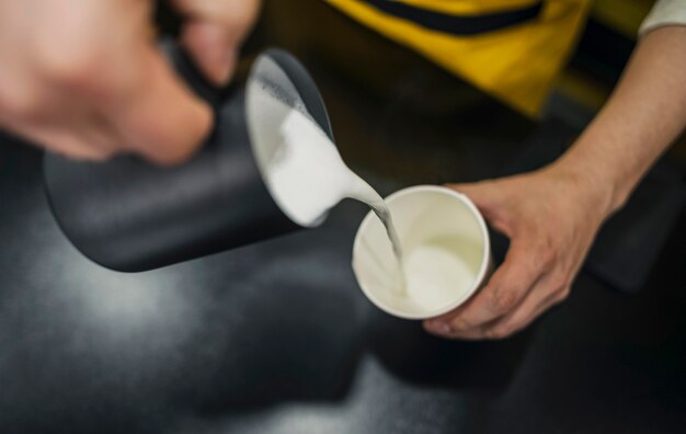 Alto ángulo de barista macho vertiendo leche en taza