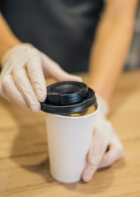 Alto ángulo de barista manipulando la taza de café con guantes de látex