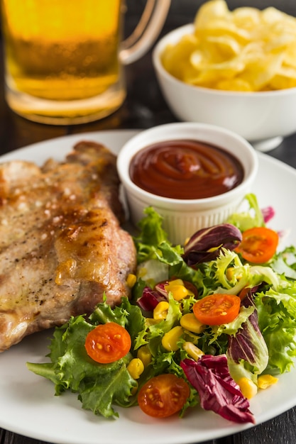 Alto ángulo de bistec en plato con ensalada y cerveza