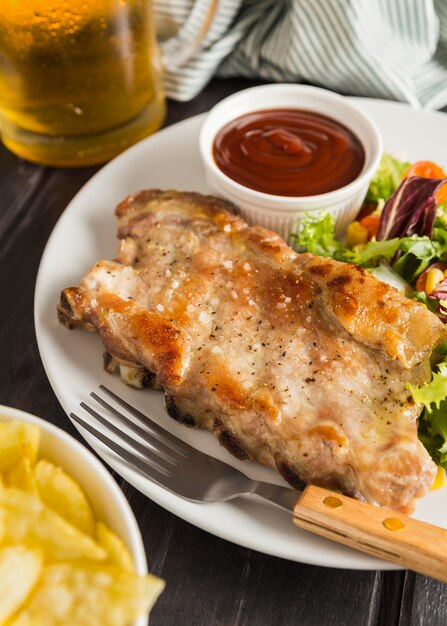 Alto ángulo de bistec en un plato con salsa de tomate y vaso de cerveza