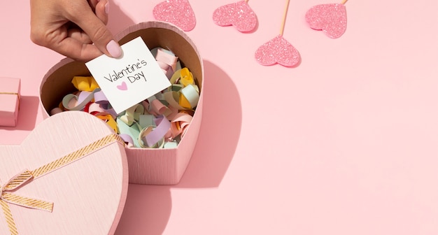 Foto gratuita alto ángulo de caja de hojalata en forma de corazón con confeti y tarjeta del día de san valentín en manos de mujer