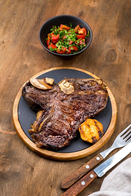 Alto ángulo de filete con ensalada y cubiertos.