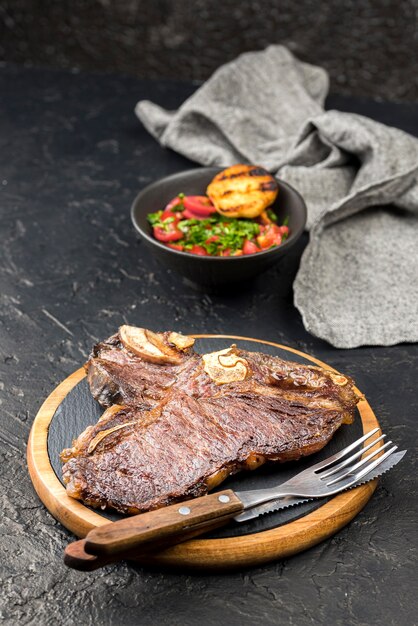 Alto ángulo de filete con ensalada y cubiertos.