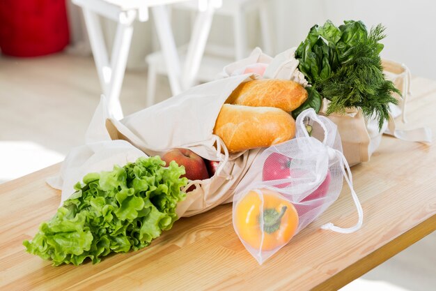 Alto ángulo de frutas y verduras en la mesa con bolsas reutilizables.