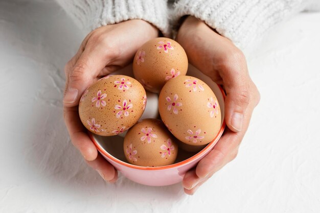 Alto ángulo de huevos de Pascua decorados en un recipiente sostenido por las manos