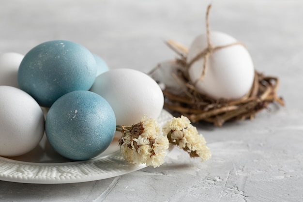 Alto ángulo de huevos de pascua en nido de pájaro con plato y flores