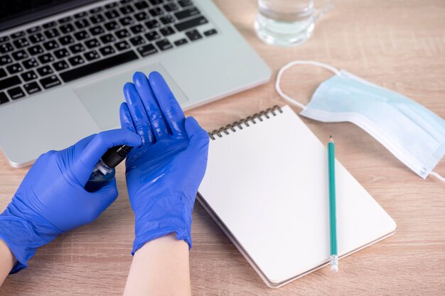 Alto ángulo de manos con guantes quirúrgicos con desinfectante de manos junto al escritorio