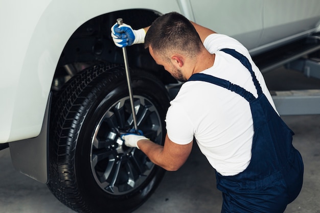 Alto ángulo mecánico masculino cambiando las ruedas del coche