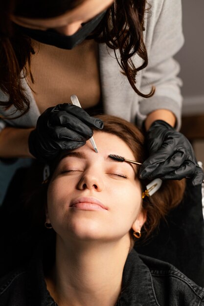 Alto ángulo de médico femenino haciendo un tratamiento de cejas para mujer