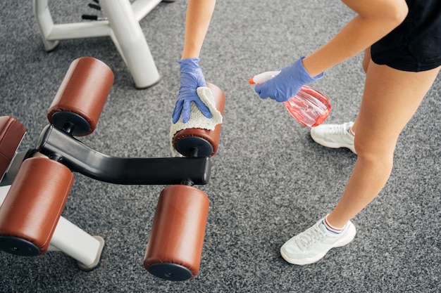 Alto ángulo de mujer con guantes en el equipo de desinfección de gimnasio