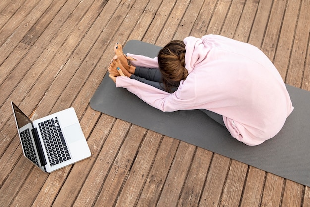 Alto ángulo de mujer con laptop haciendo yoga al aire libre