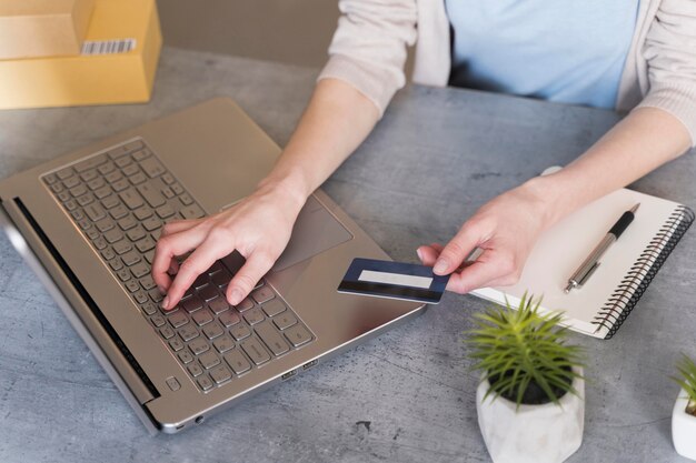 Alto ángulo de mujer que trabaja en la computadora portátil con tarjeta de crédito y planta